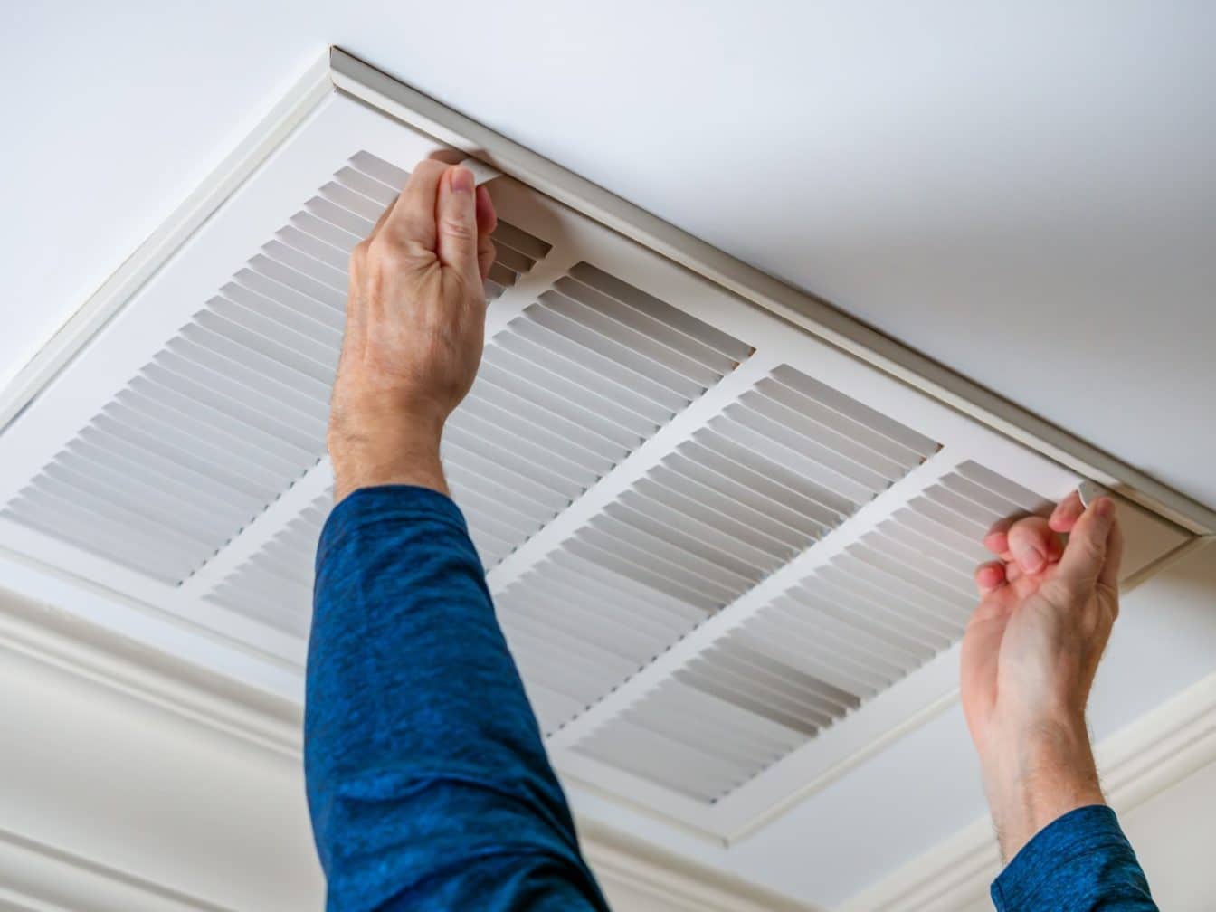 Man opening ceiling air vent to replace dirty HVAC air filter. H